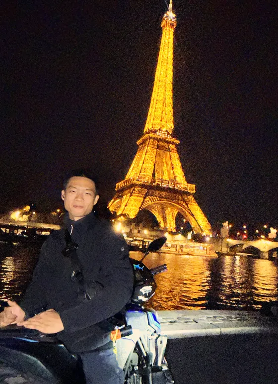 Pengyu Jie with his motorcycle at the Eiffel Tower at night